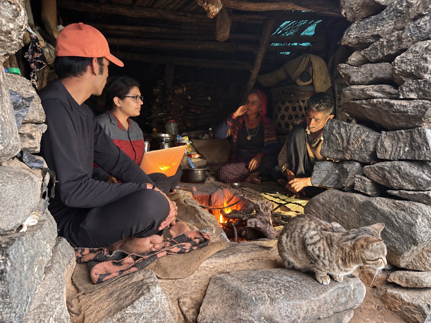 Researchers sitting with a family beside the hearth in a stone shelter, documenting local knowledge